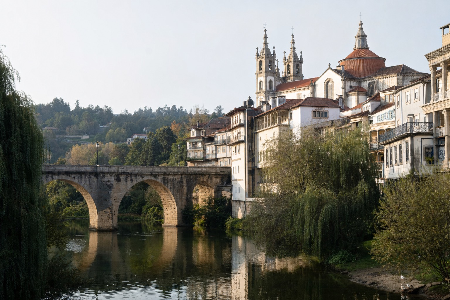 Granite arched bridge over the calm Tamega river in Amarante with a baroque church tower and balconied old town houses behind it