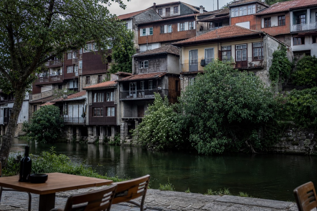 Balconied townhouses stacked above the tree-lined Tamega river in Amarante's old town on a still morning