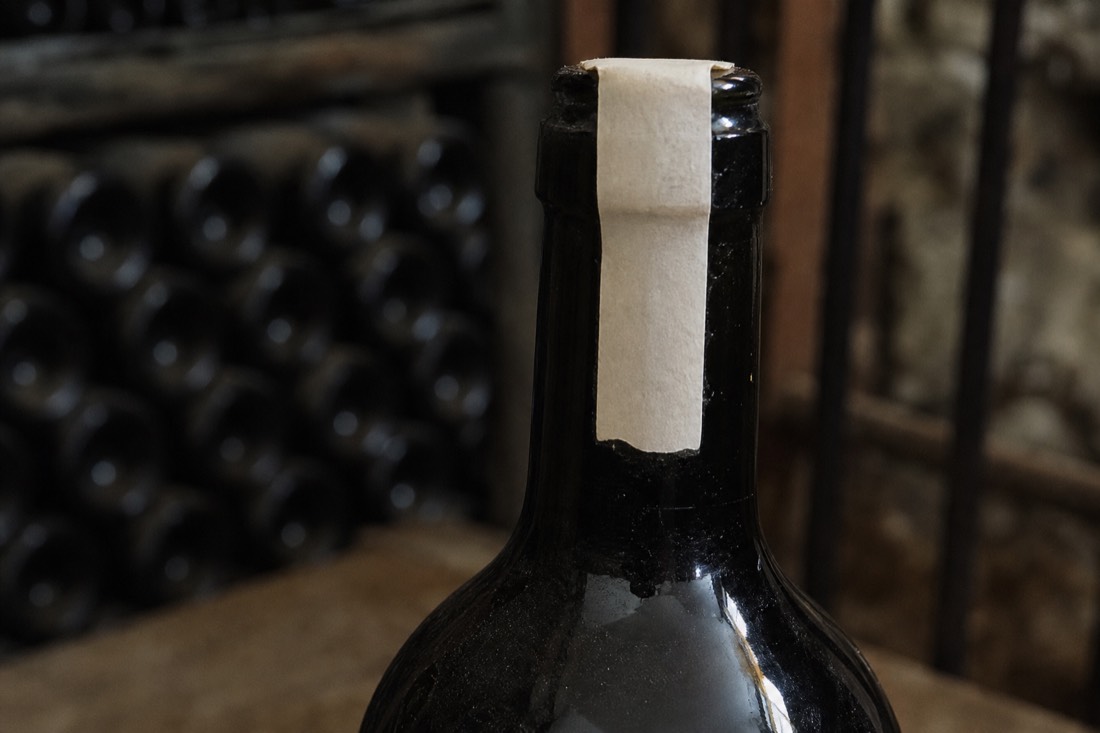 Close view of a dark port bottle neck with a paper seal band over the capsule, label turned away