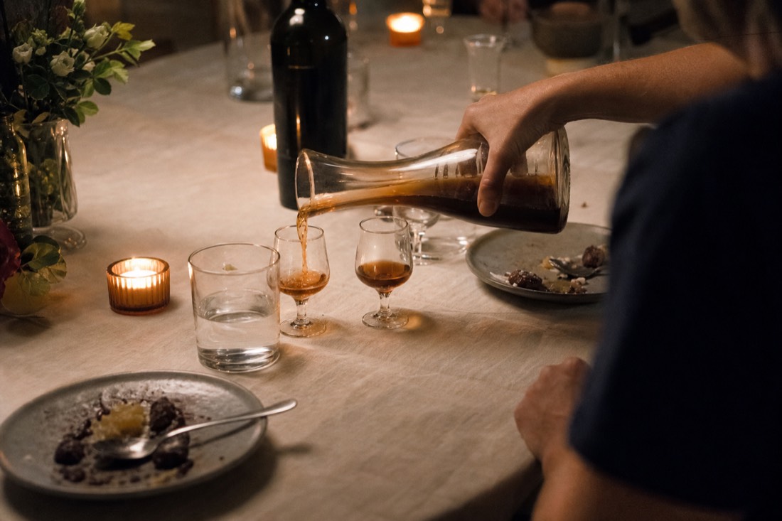 Tawny port being poured into small glasses on a candlelit dinner table with dessert plates