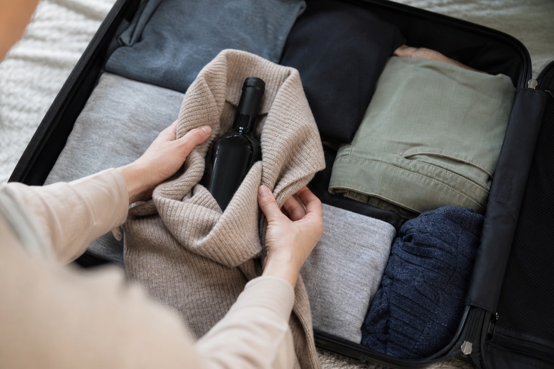 Wine bottle being wrapped in clothing inside a suitcase padded with soft garments