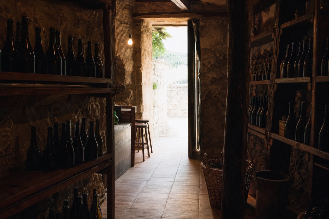 Small stone-walled quinta shop with wooden shelves of wine bottles and afternoon light through the doorway