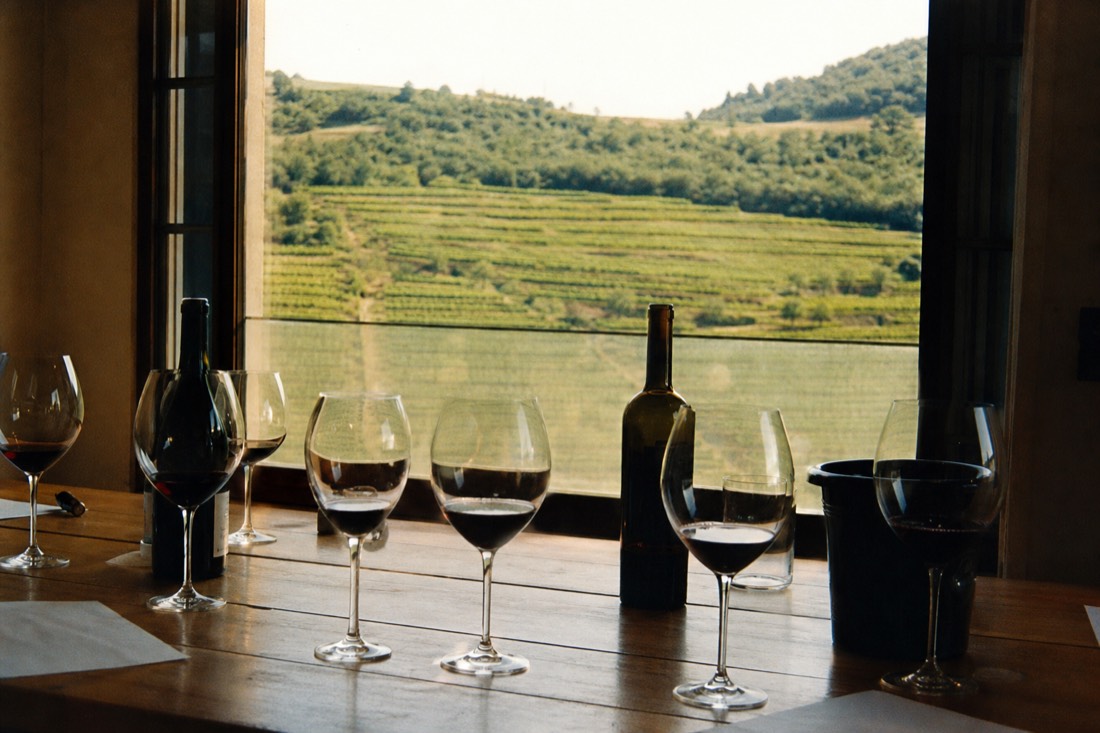 Tasting table set with several red wine glasses and a view of vineyard terraces through an open window