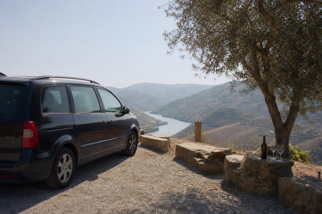 Small tour van parked at a vineyard viewpoint overlooking the winding Douro river on a bright day