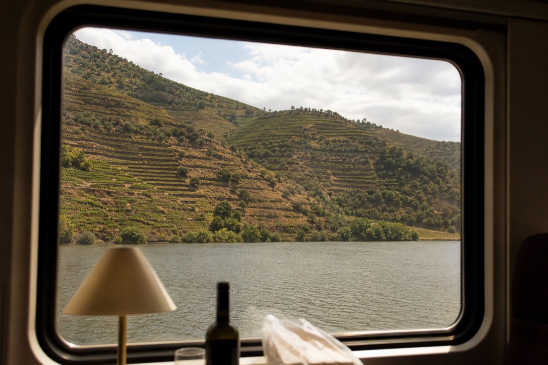 Regional train window framing the Douro river and vine terraces gliding past close to the waterline