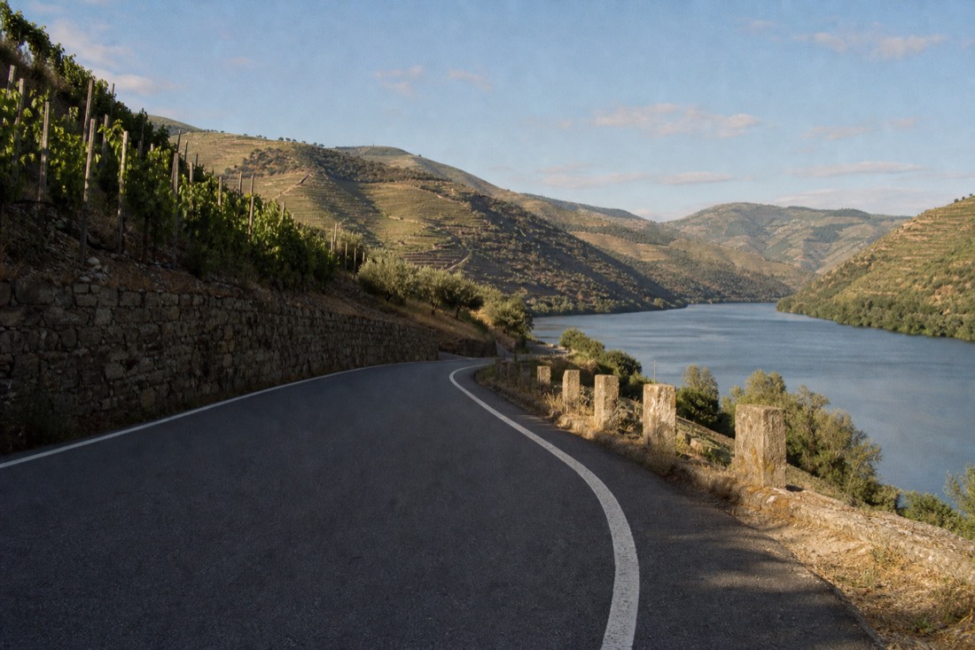 Empty winding N222 road curving along the Douro river between stone terraces in late afternoon light