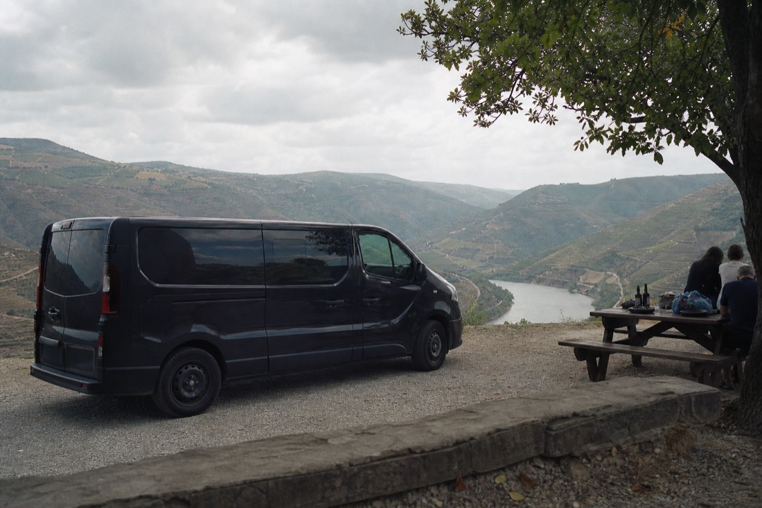 Small tour van parked at a gravel viewpoint pullout above terraced Douro vineyards while the valley opens below