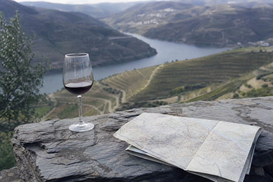 Wine glass and folded paper map on a stone ledge overlooking terraced vineyards in soft afternoon light