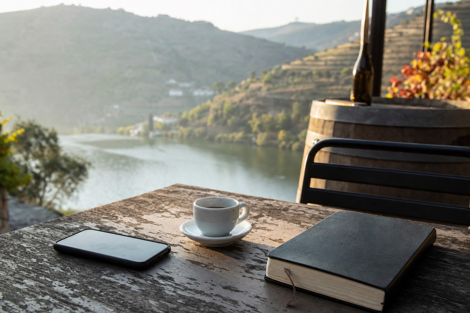 Phone lying face down beside an espresso and a notebook on a cafe table with the Douro river blurred in the background
