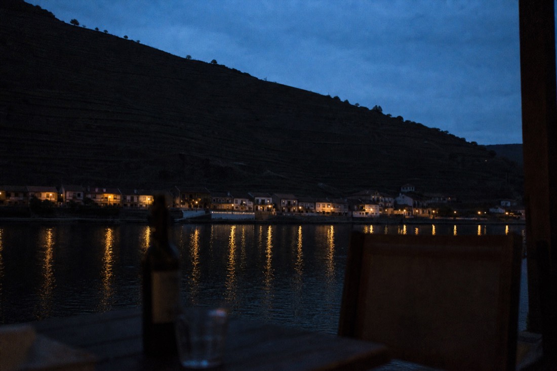 Dusk over the Douro river with lights of a small riverside town and dark terraced slopes above