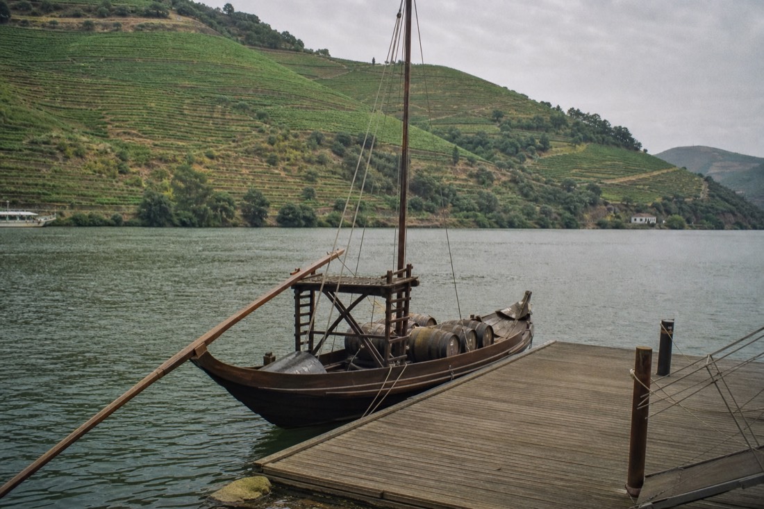 Traditional wooden rabelo style boat waiting at a small pier on the Douro river beneath terraced hills