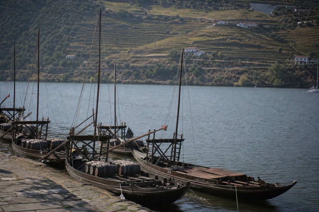 Wooden rabelo boats moored along a small river quay with vineyard slopes rising behind them