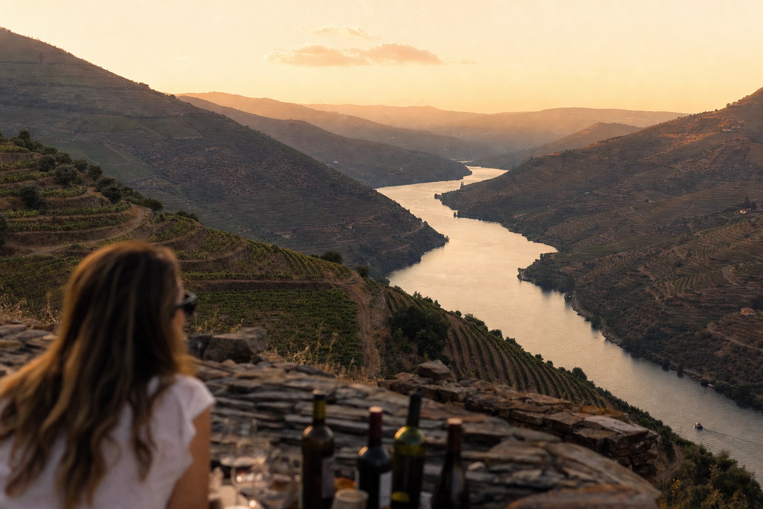 Terraced Douro vineyards stepping down to the river at golden hour with hills fading into haze behind