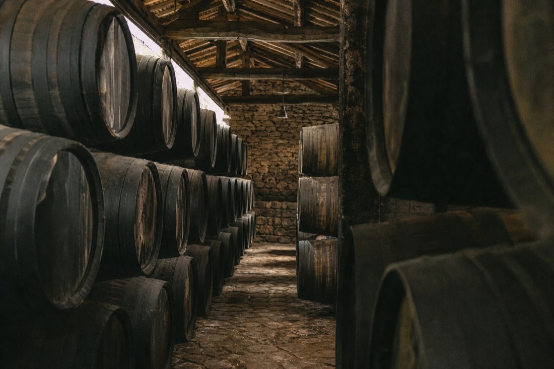 Rows of old wooden barrels resting in a dim Port wine cellar with dark staves and stone floor