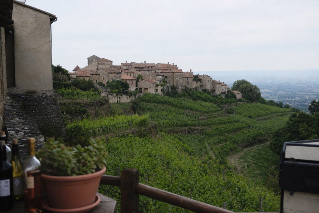 Small stone village of terracotta roofs perched on a hillside above rows of vineyard terraces