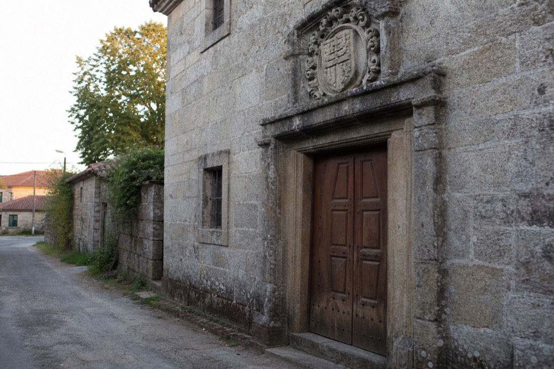Old granite manor house with a carved stone coat of arms above a heavy wooden door in a quiet village