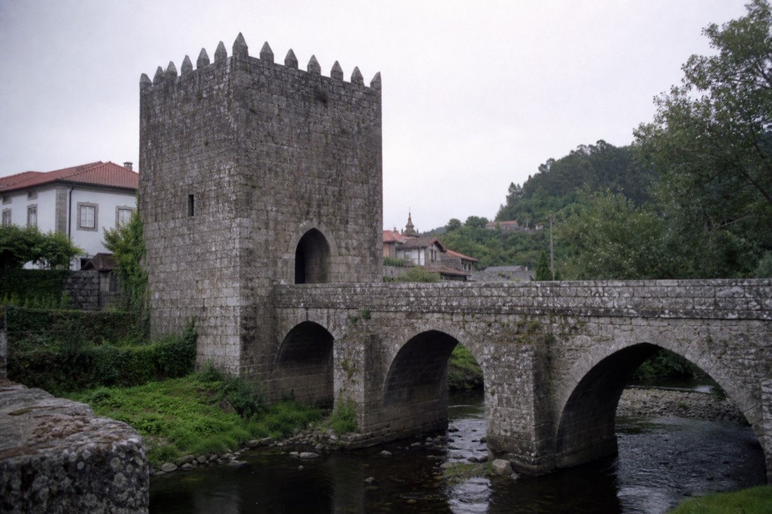 Old stone bridge with a fortified tower spanning a small river beside a historic village