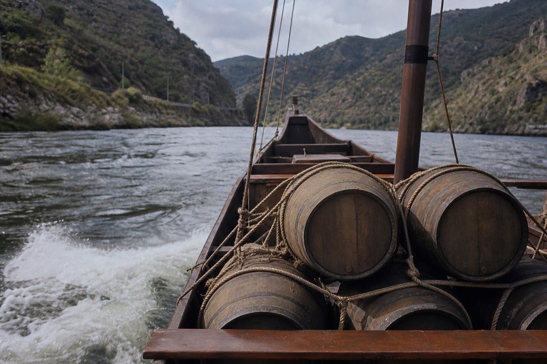 Wooden port barrels stacked and lashed on the deck of a rabelo boat on a fast stretch of river between steep hills