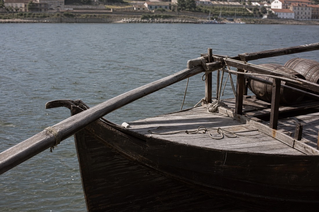 Close view of a wooden rabelo boat hull and long steering oar over the stern, ropes coiled on the deck