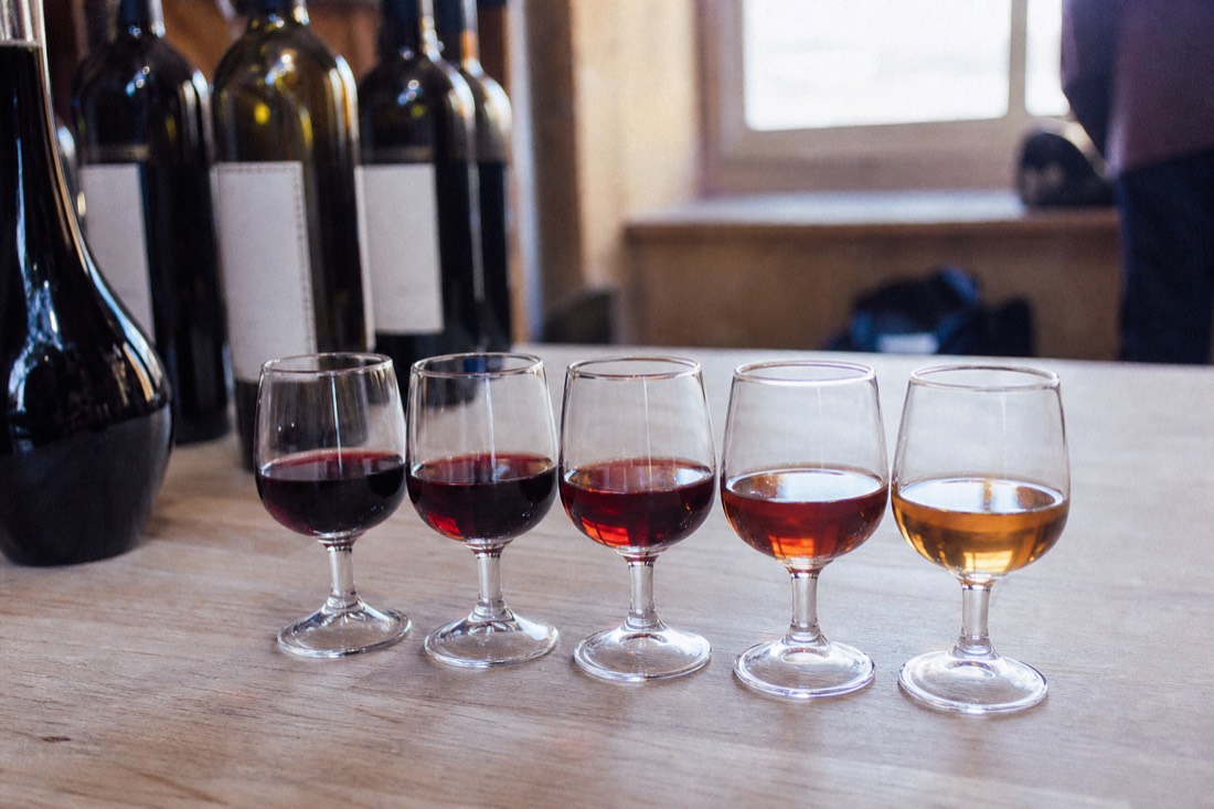 Small port glasses arranged in a line showing the color shift from deep ruby red to pale amber brown
