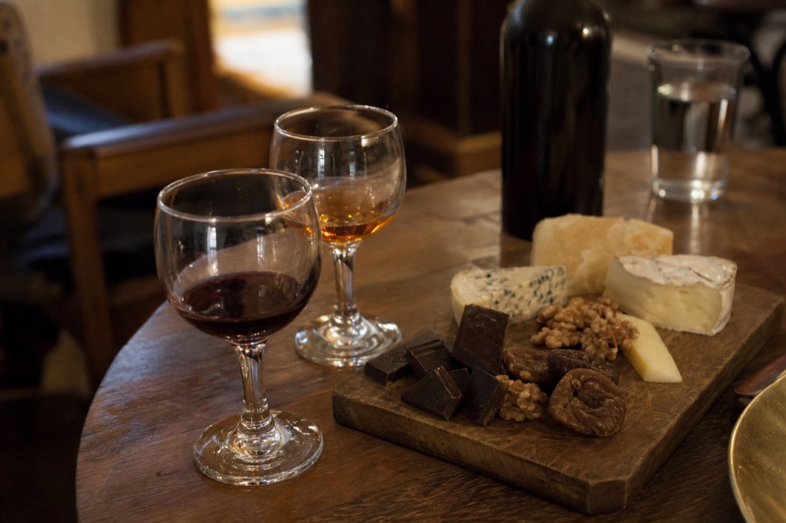 Cheese board with dark chocolate, walnuts and dried figs beside glasses of tawny and ruby port