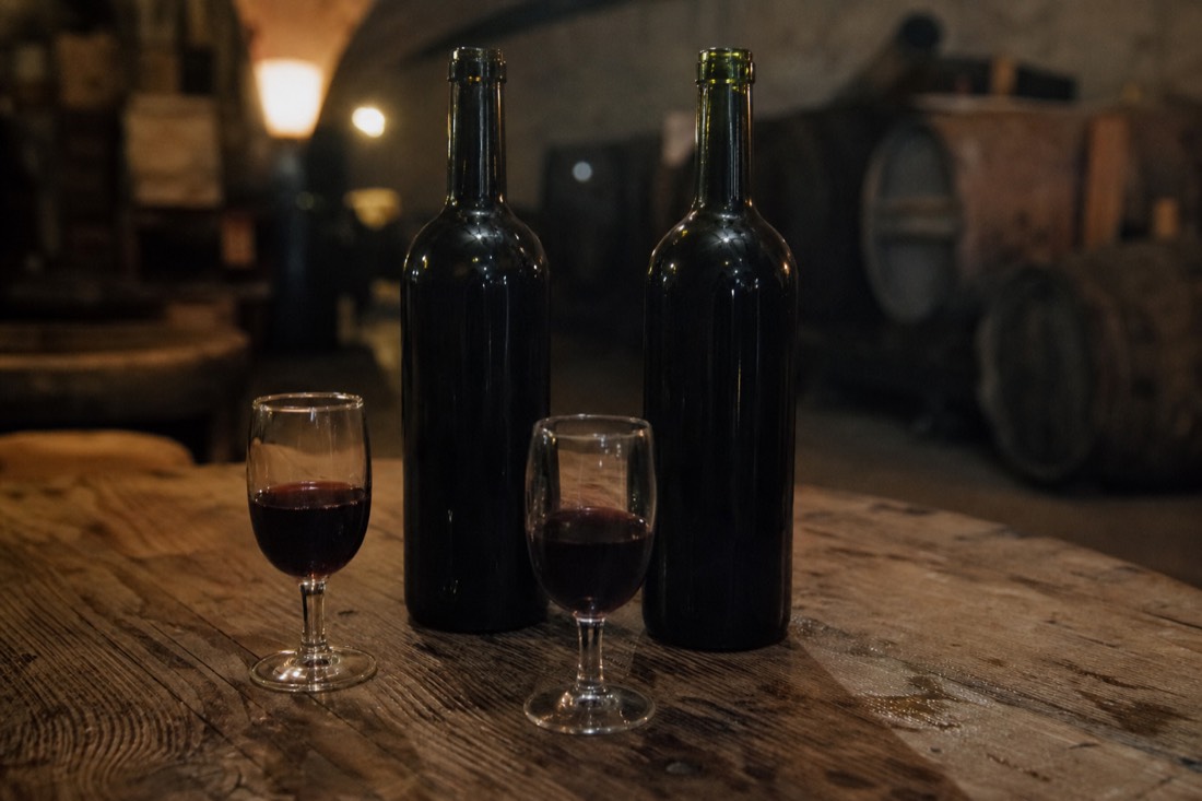 Two open port bottles beside filled glasses on a worn wooden tasting table in warm cellar light