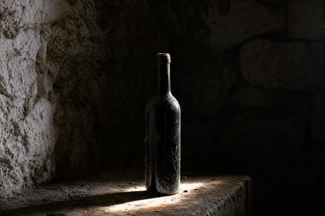Single dusty dark bottle of aged port standing in the beam of light in a cool stone cellar