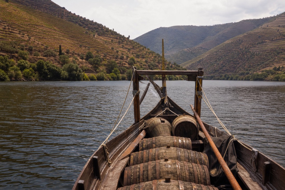 Traditional wooden rabelo boat on the calm Douro river with steep terraced vineyard slopes rising on both banks