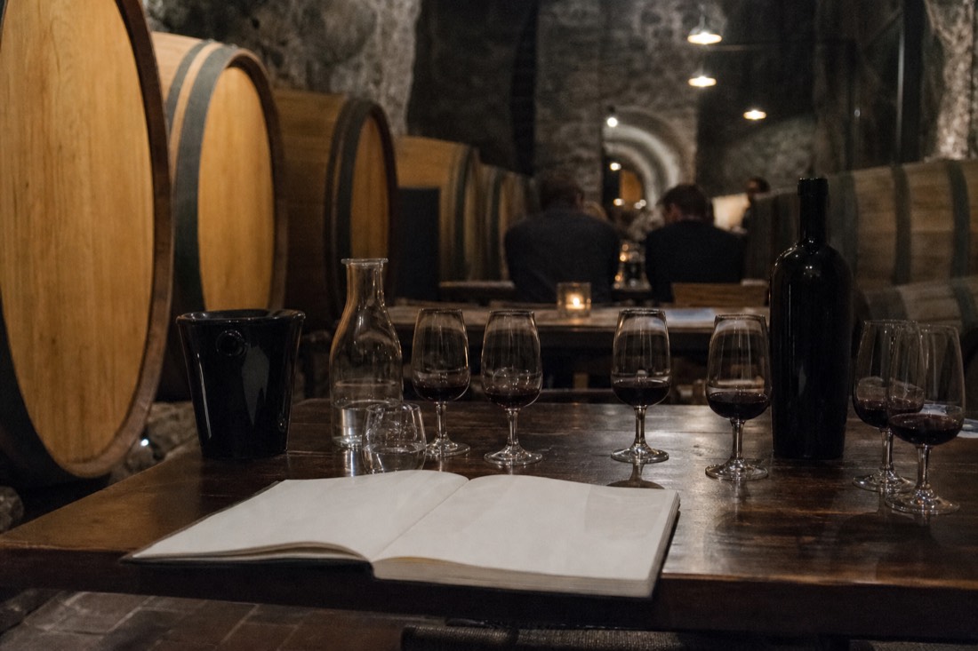 Tasting table with small port glasses and a notebook in a cool stone cellar lined with wooden barrels