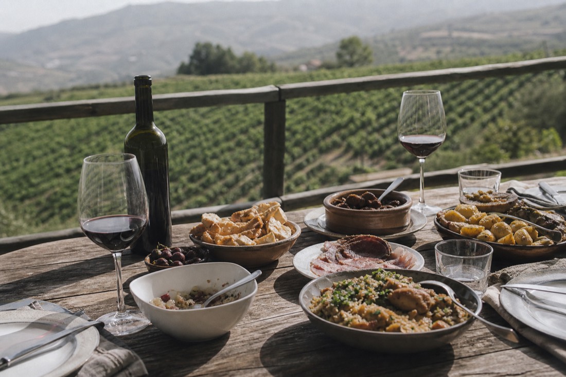 Rustic table laid with regional Portuguese dishes and glasses of red wine on a vineyard terrace