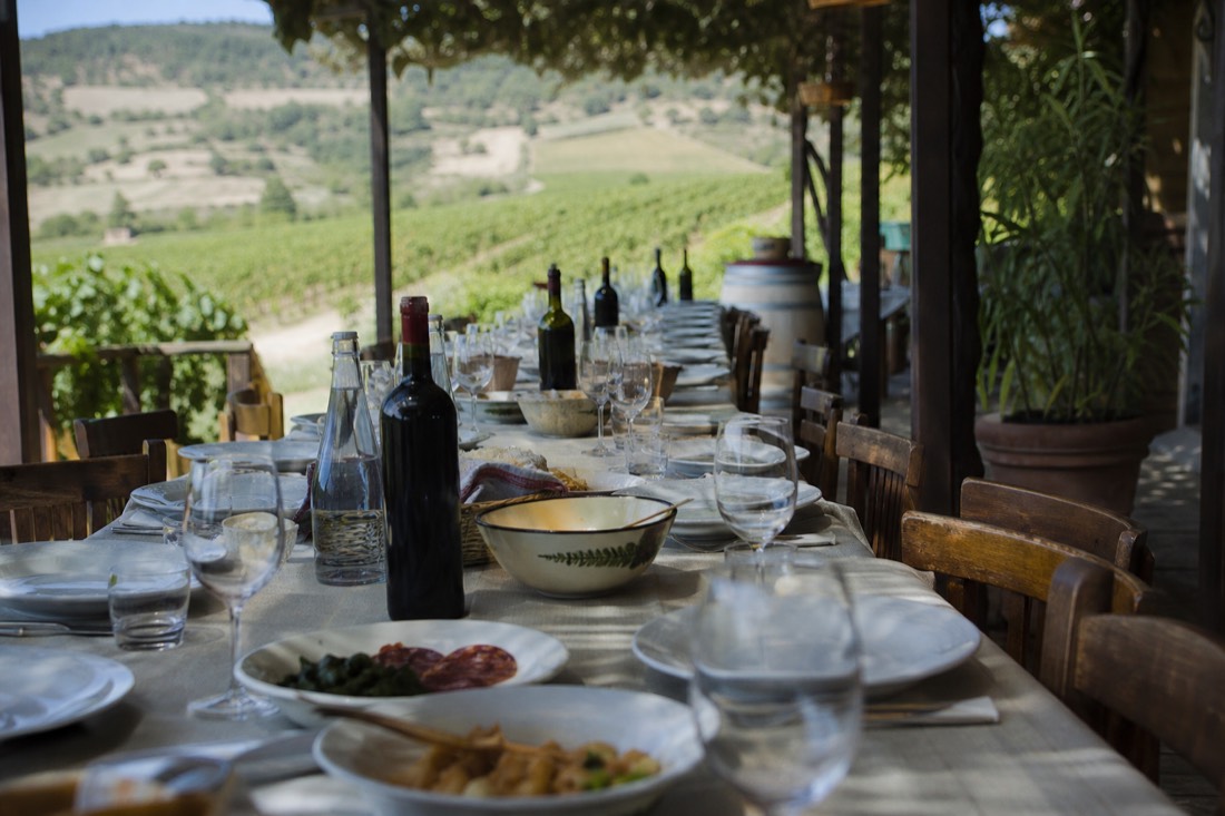 Long table set for a group lunch with regional dishes and wine bottles on a shaded vineyard terrace