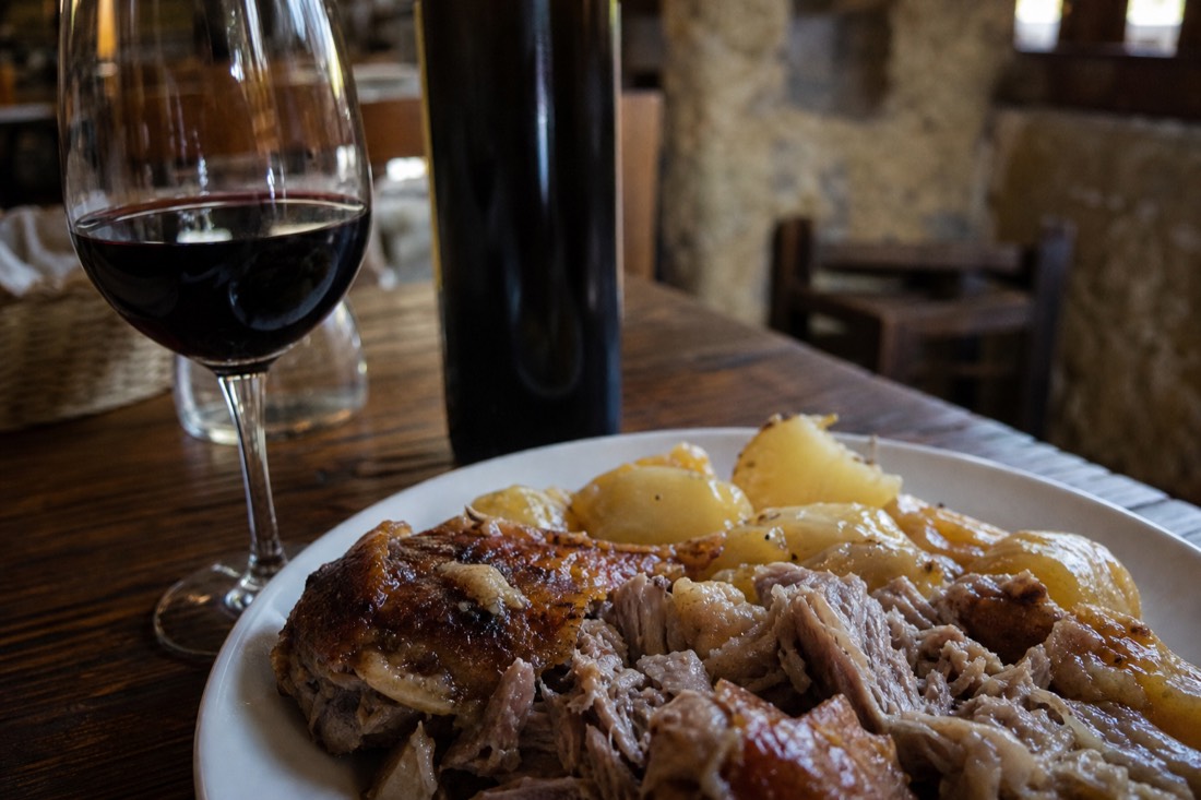 Plate of slow roasted regional meat with potatoes beside a glass of dark Douro red wine