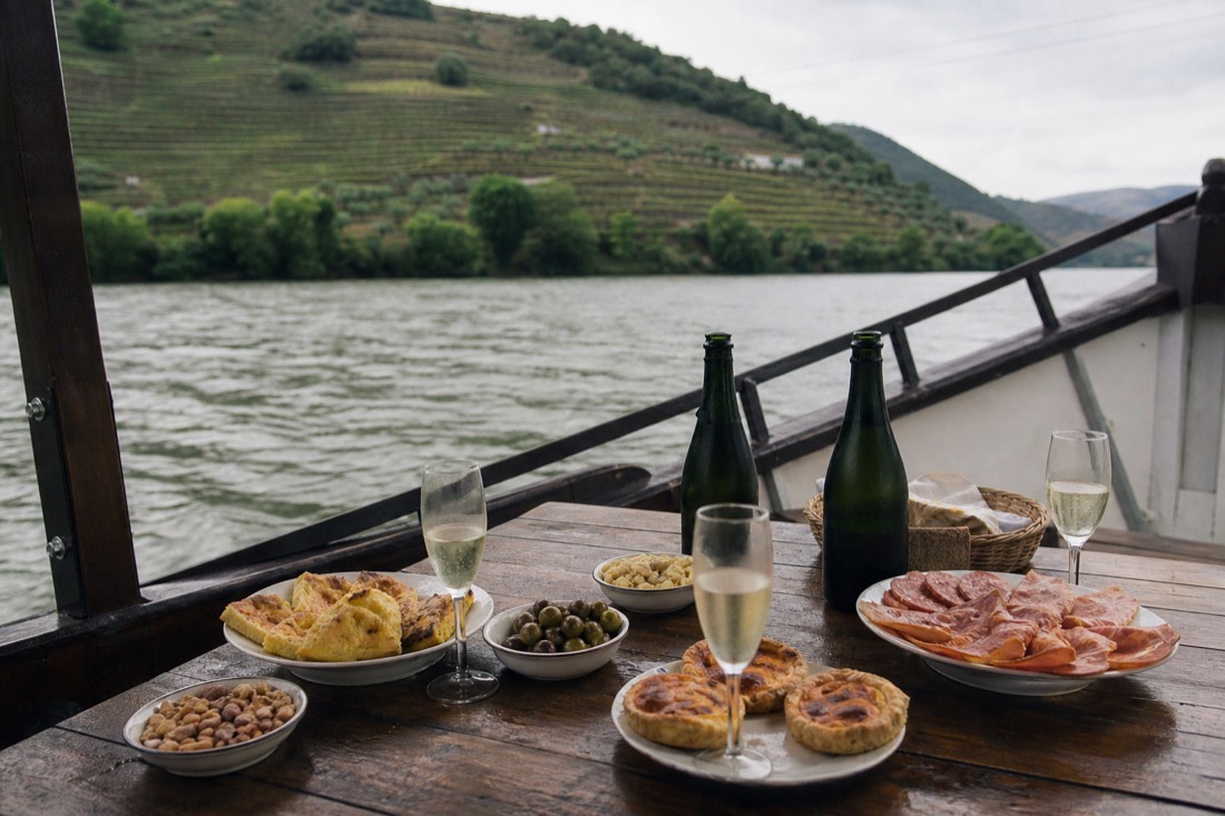 A private boat on the Douro with a spread of tapas and glasses on a table aboard, vineyards beyond