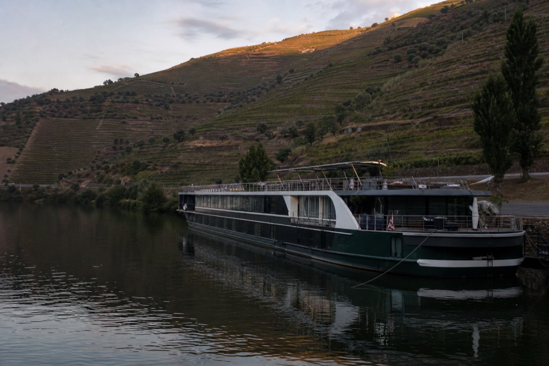 A long river ship moored on a quiet stretch of the upper Douro beneath terraced slopes at dusk