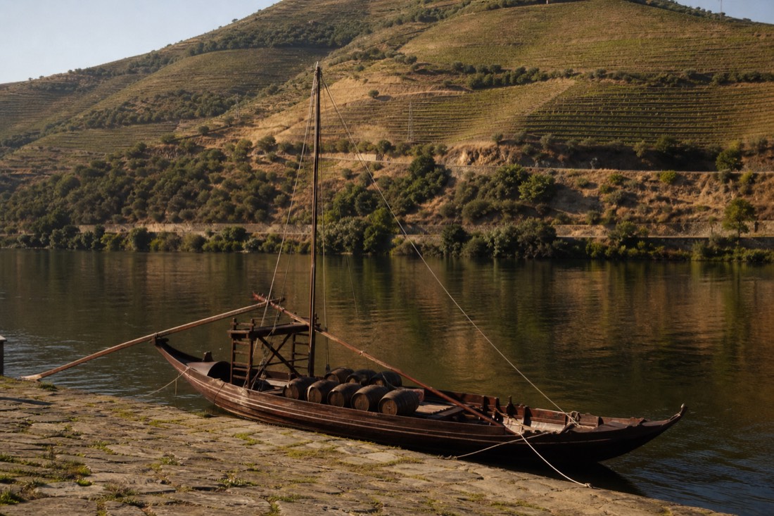 A small rabelo cruise boat waiting at the Pinhao quay in warm late-afternoon light with vineyards rising behind