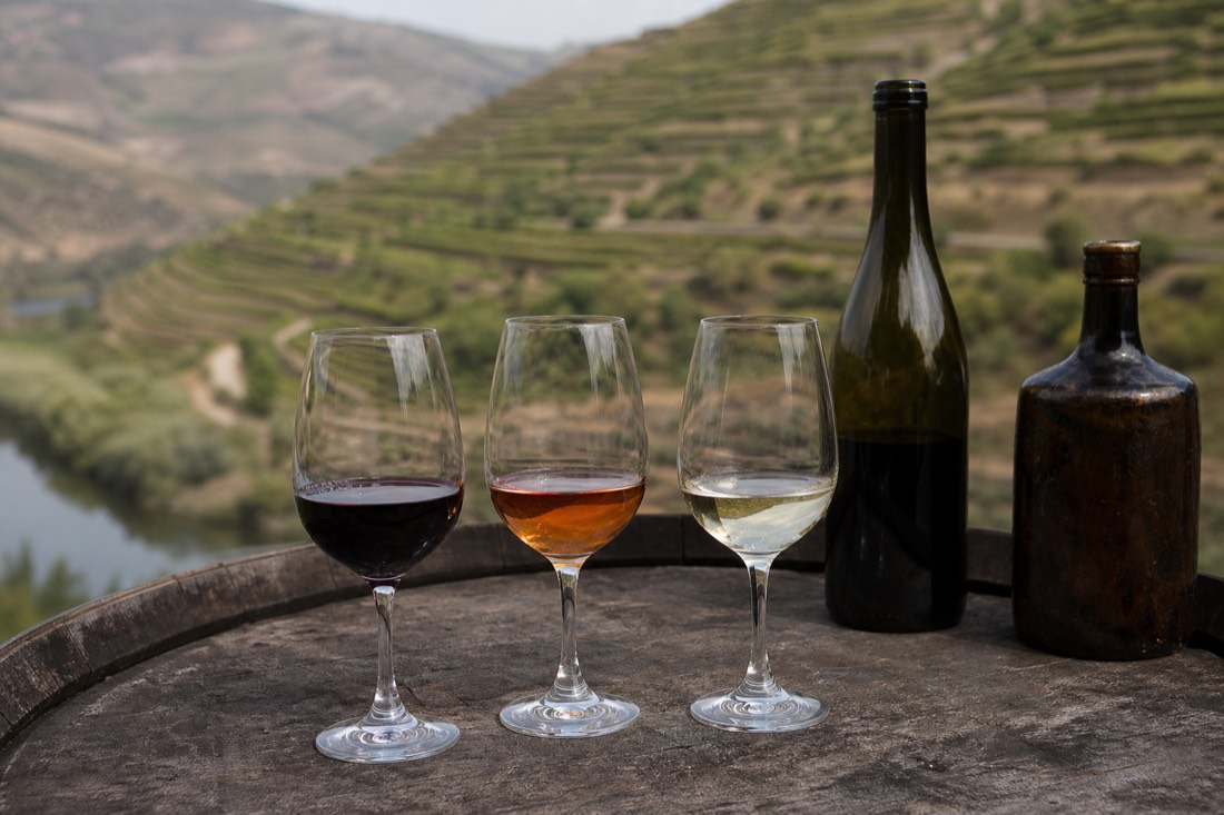 Three wine glasses with different Douro wines lined up on a barrel top against a vineyard backdrop
