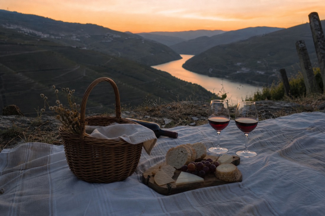 Sunset picnic blanket with wine glasses and regional food overlooking terraced Douro vineyards at dusk