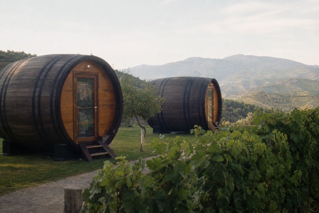 Giant wine-barrel-shaped guest cabins on a lawn beside vineyards at a Douro wine estate