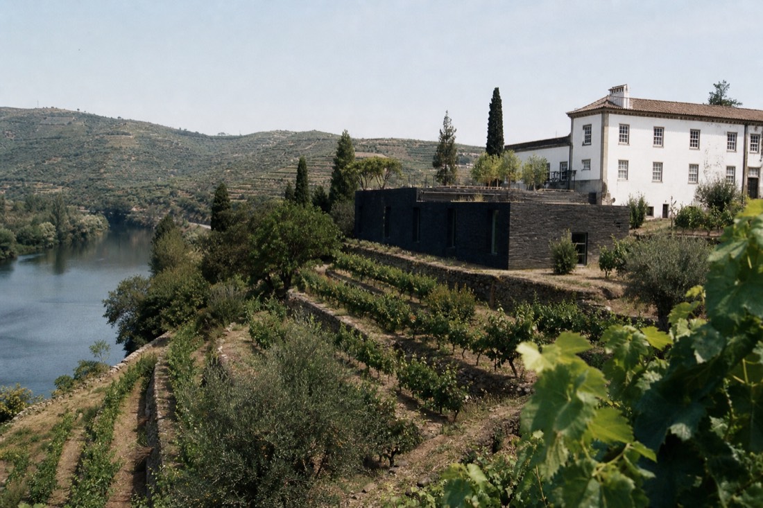 Modern schist-stone winery wing beside an old manor house among vineyard terraces near a river