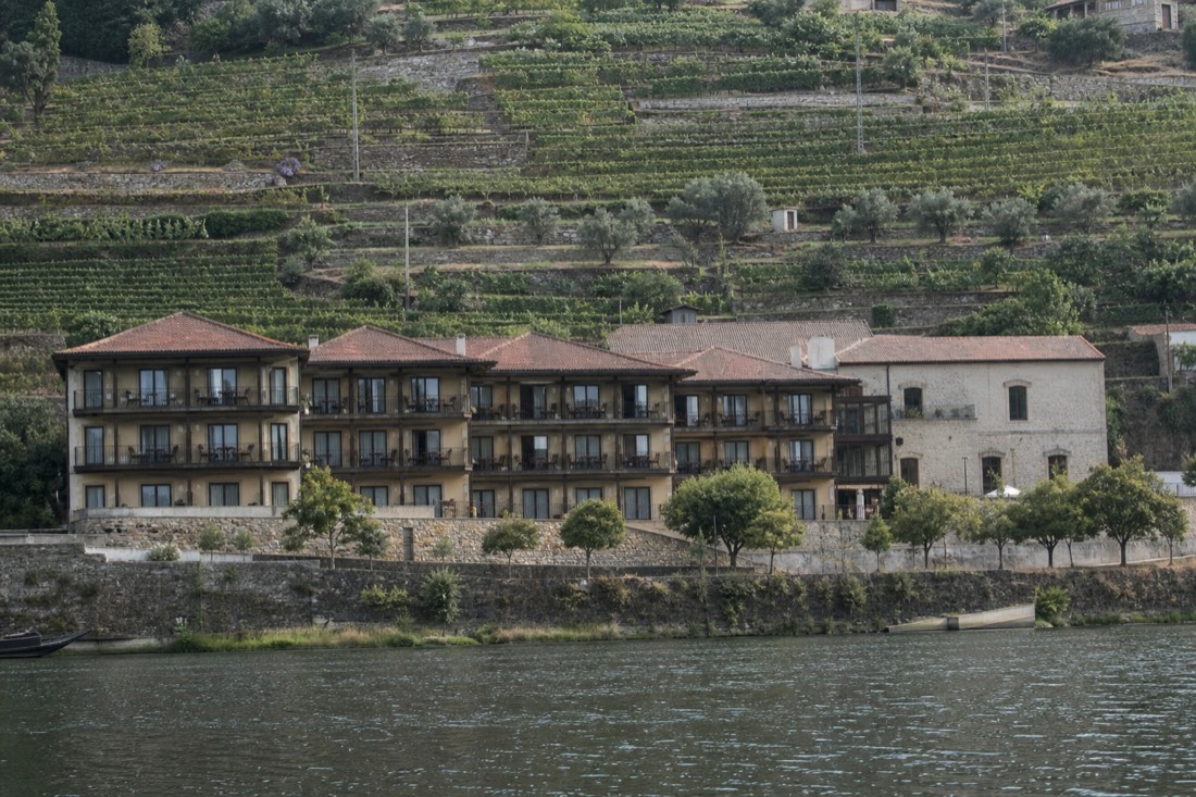 A long low riverfront hotel on a quay with balconies facing the Douro and terraced hills behind
