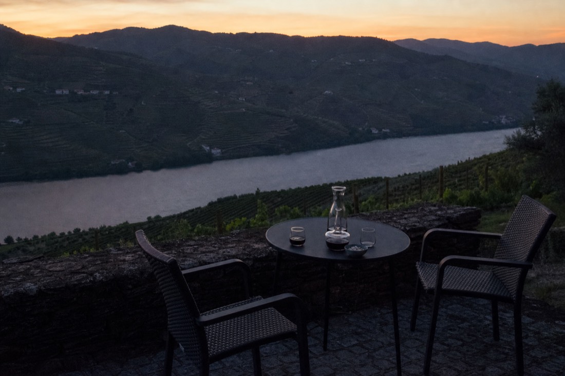 A quinta guest terrace with empty chairs and a small table overlooking terraced vineyards at dusk