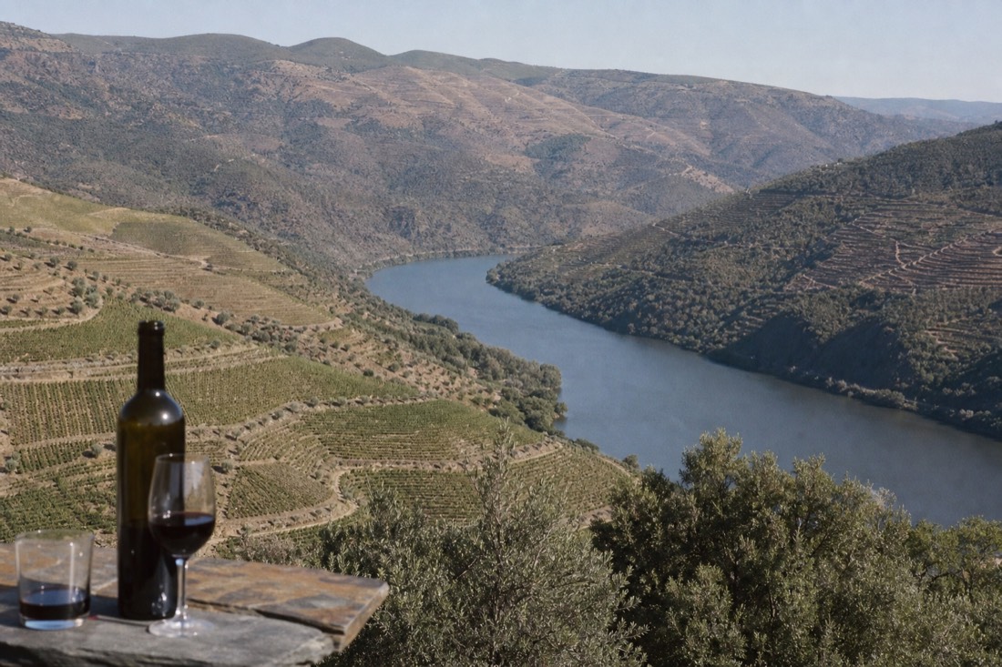 The Douro river winding between three zones of terraced hillside, greener slopes downstream giving way to drier bare ridges upstream
