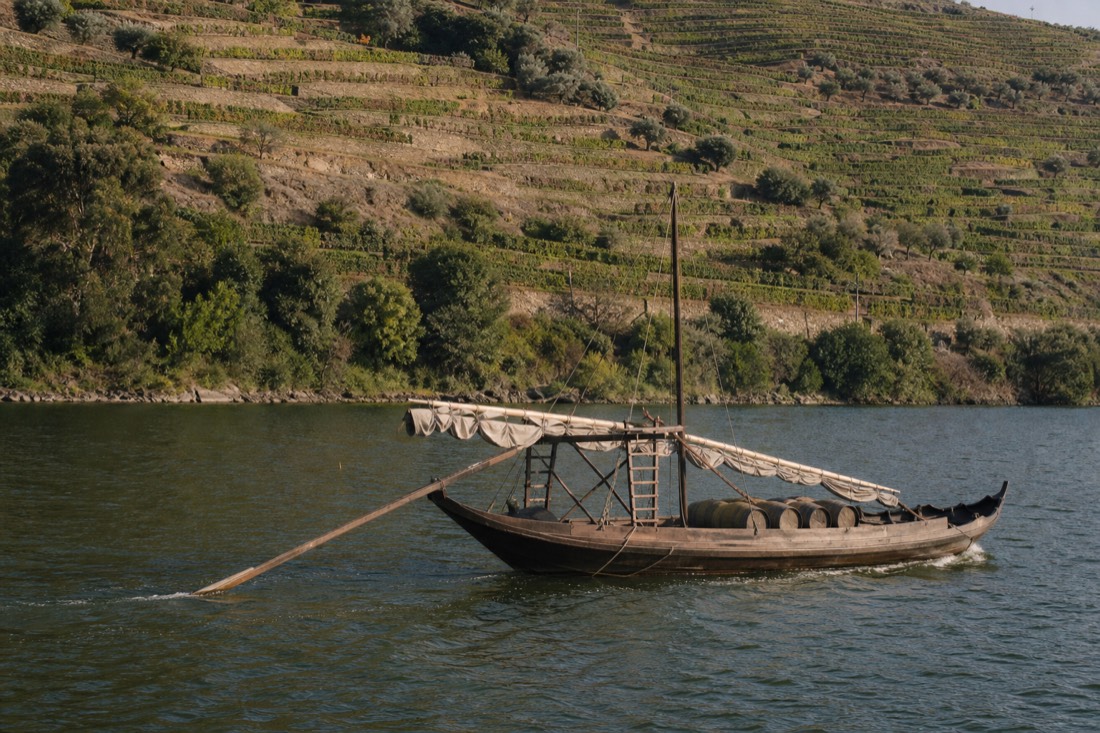 Wooden rabelo boat cutting calm green water at Pinhao with terraced hills behind