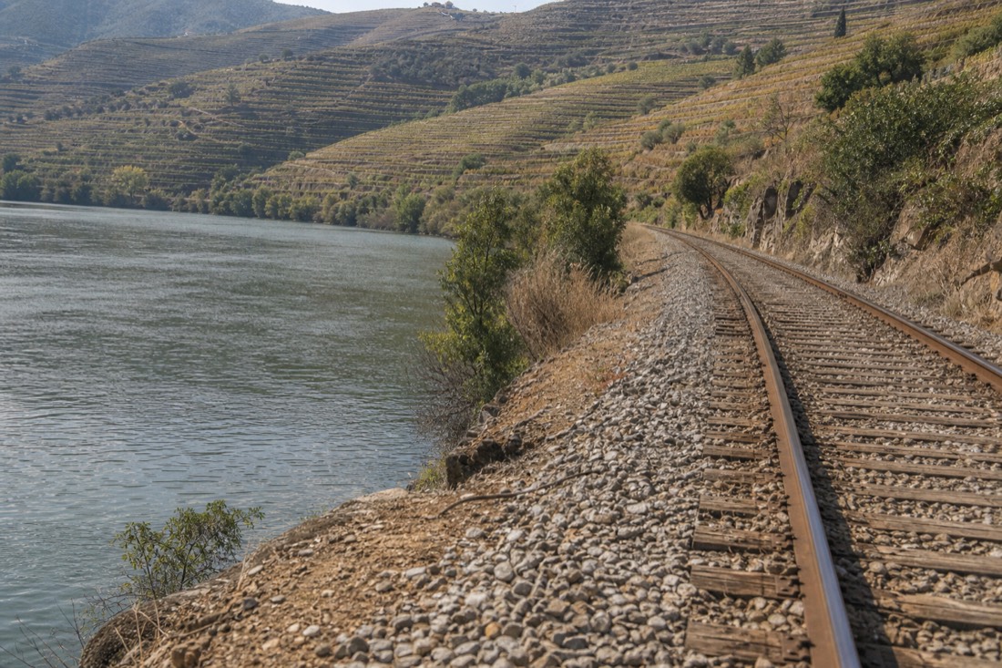 Single railway track running beside the Douro River below steep terraced hillsides