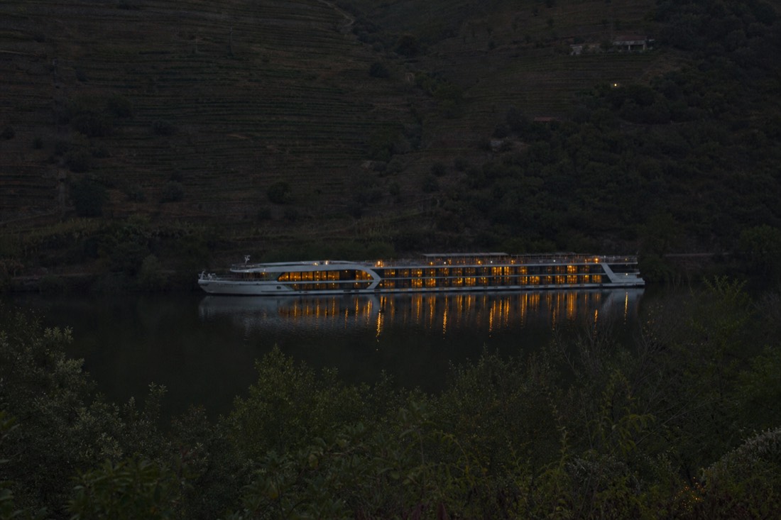Long river ship moored on a quiet stretch of the upper Douro beneath terraced slopes at dusk
