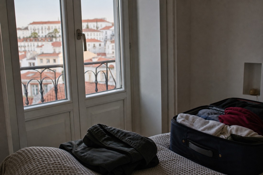 Packed suitcase and jacket by a Lisbon apartment window at first light before a long travel day