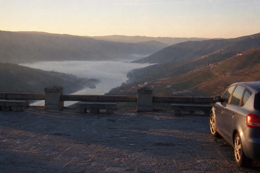 Empty early-morning miradouro viewpoint over Douro terraces with a single parked car and soft valley mist