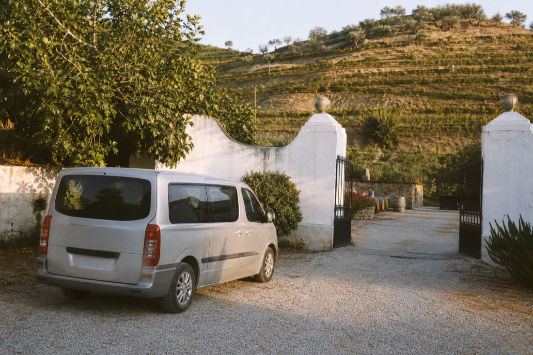 Small tour van waiting outside a whitewashed quinta gate while afternoon light falls on vineyard terraces