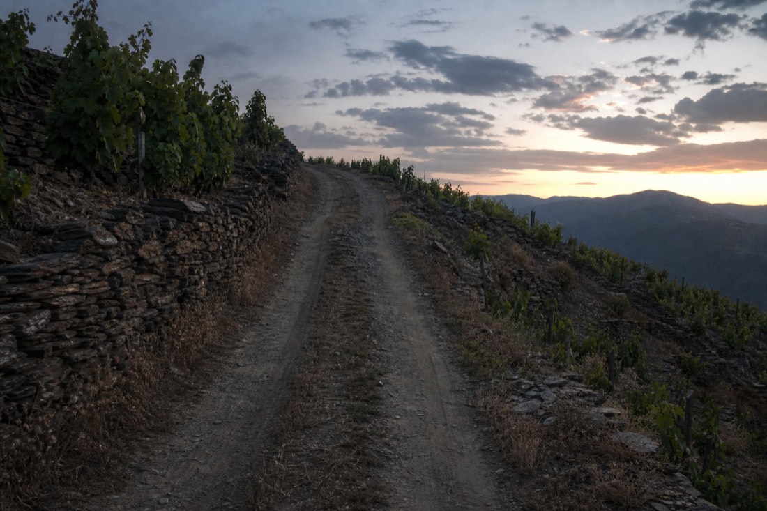 Dusty 4x4 track winding up through steep schist terraces toward the evening sky