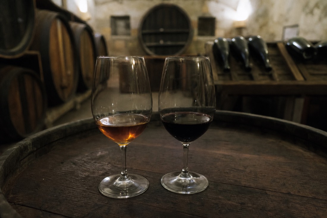 Two glasses side by side on a barrel, one amber tawny port and one deep still red wine